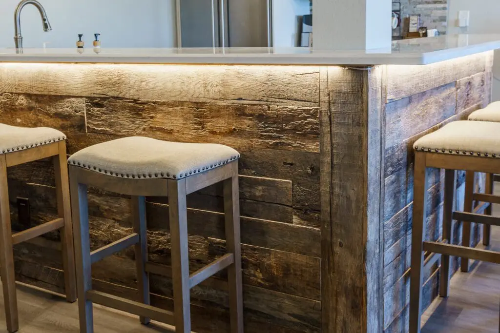 Close-up of a reclaimed barnwood basement bar front with LED under-counter lighting and nailhead barstools