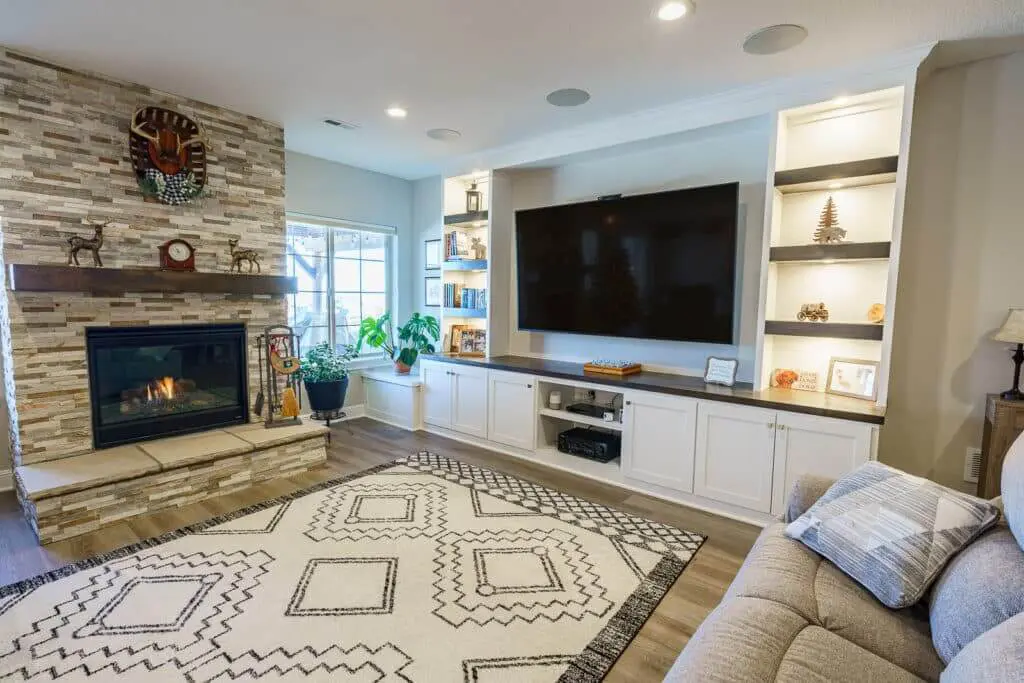 Finished basement seating area with stone fireplace, mounted TV and built-in shelving across from the bar